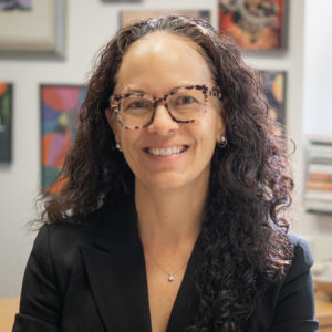 Photo of Chandra Alexandre, a woman smiling wearing glasses and black blazer.